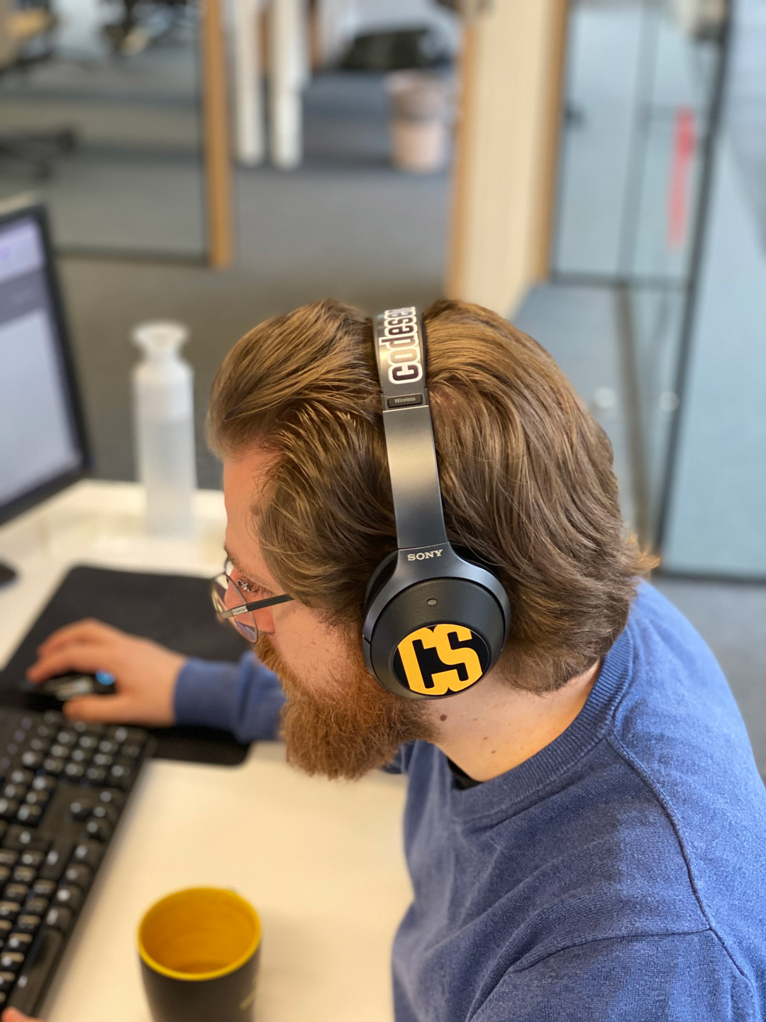 Een developer aan het werk achter zijn bureau met een koptelefoon.